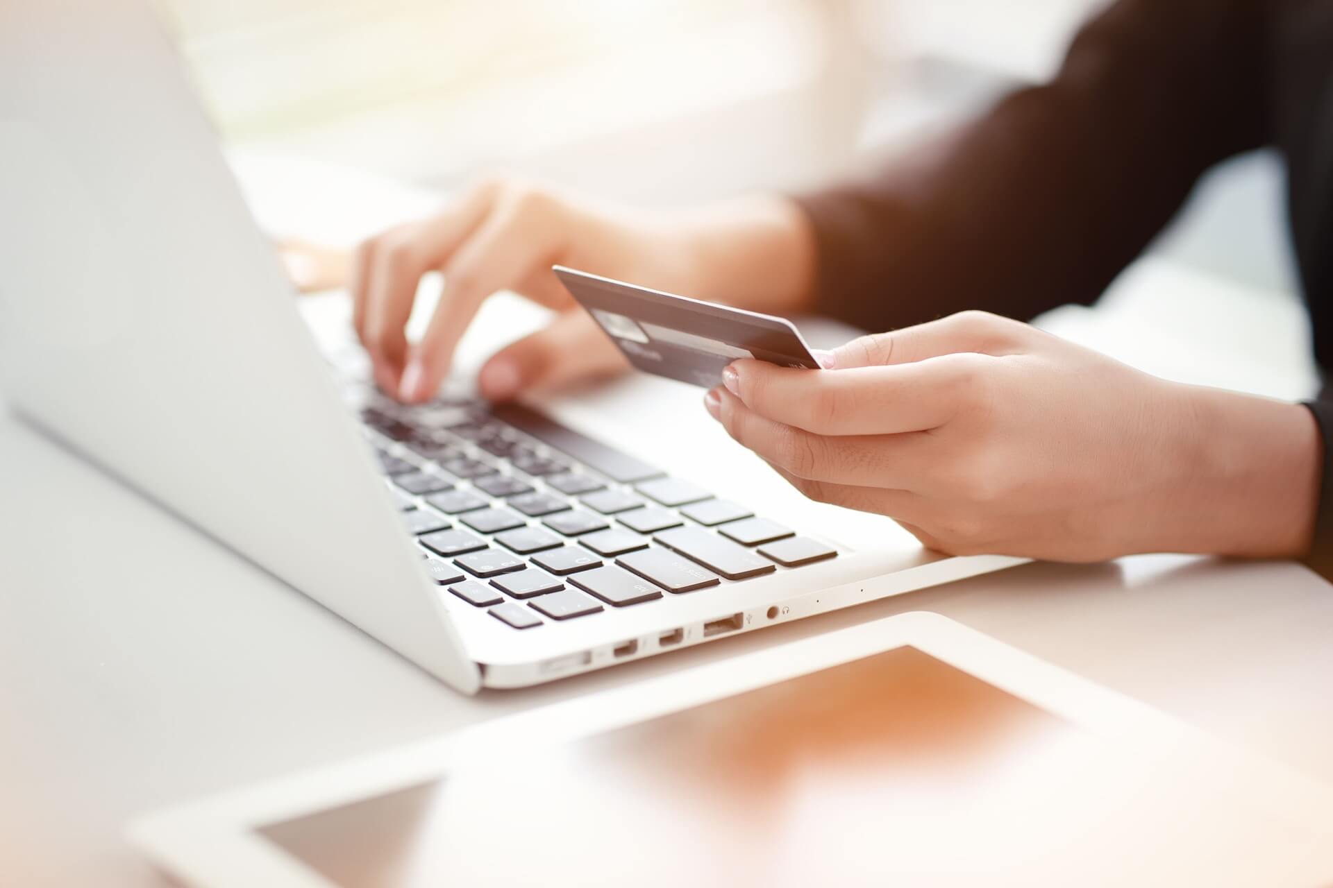 Pessoa fazendo contestação de compra pelo notebook com cartão de crédito na mão.