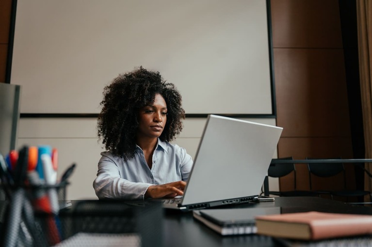 Secretária de escritório trabalhando com expressão focada em um notebook prateado.